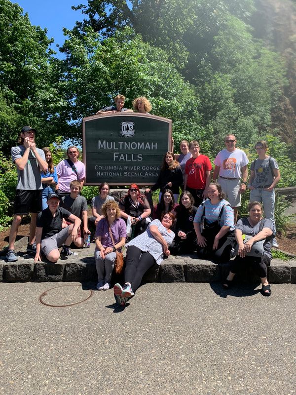 a group of youth and adults gathered next to a sign for "Multnomah Falls Columbia River Gorge National Scenic Area"