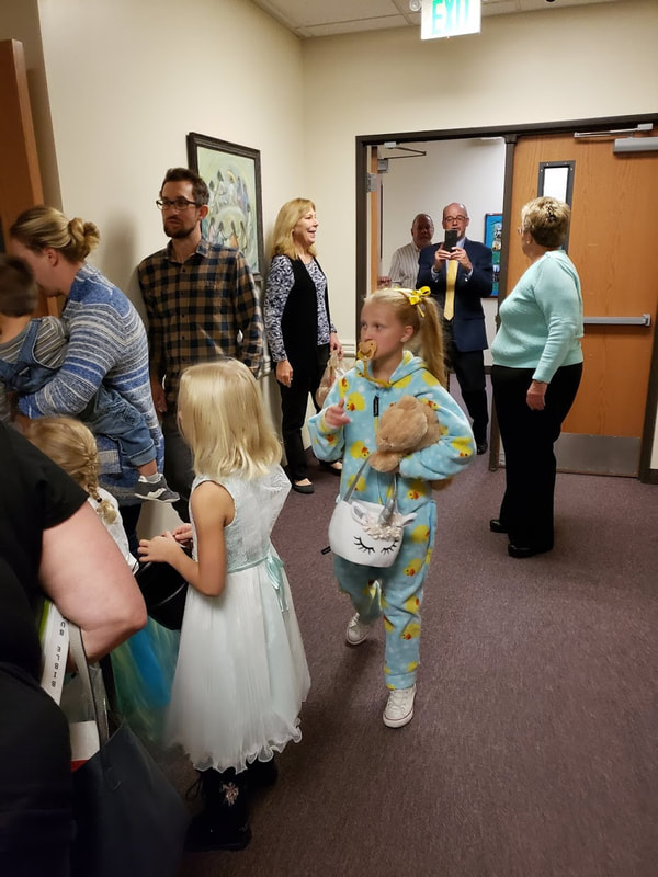 a hallway full of children in costume trick-or-treating, adults milling around, and Rev. Rusty taking a photo